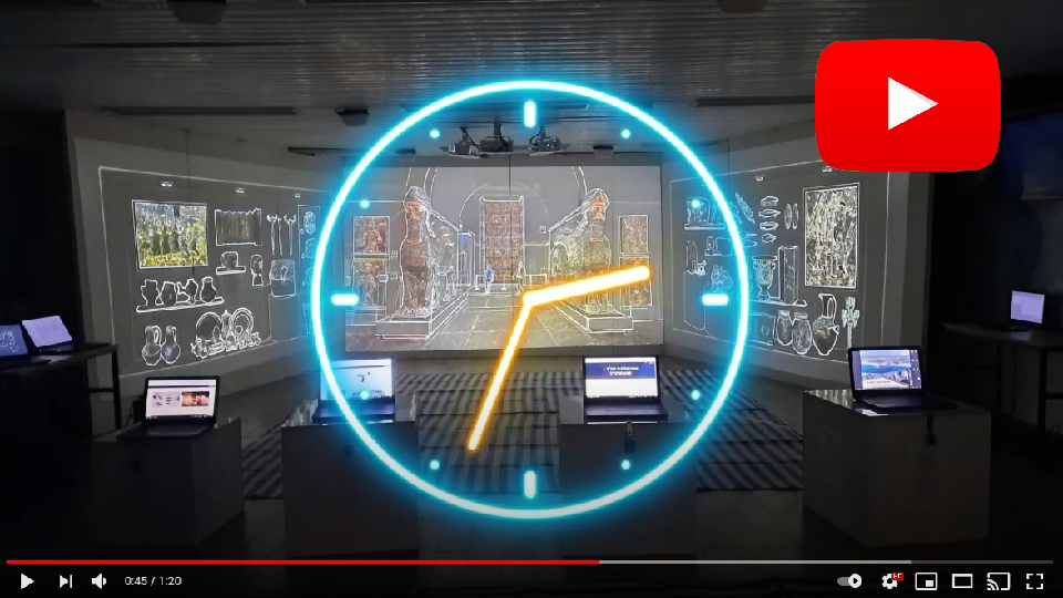 צילום מתוך סרטון של שעון זוהר על רקע חדר מוקרן באיורי כלי מוזיאון, עם מחשבים ניידים על עמודים