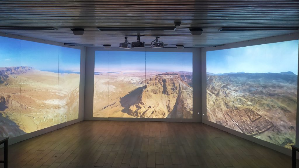 Photo of the immersive room with an aerial panorama of Masada and the surrounding desert running continuously across all three projection walls